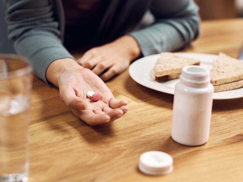 Una mujer tiene una la mano una pastilla y al lado un sandwich. 
