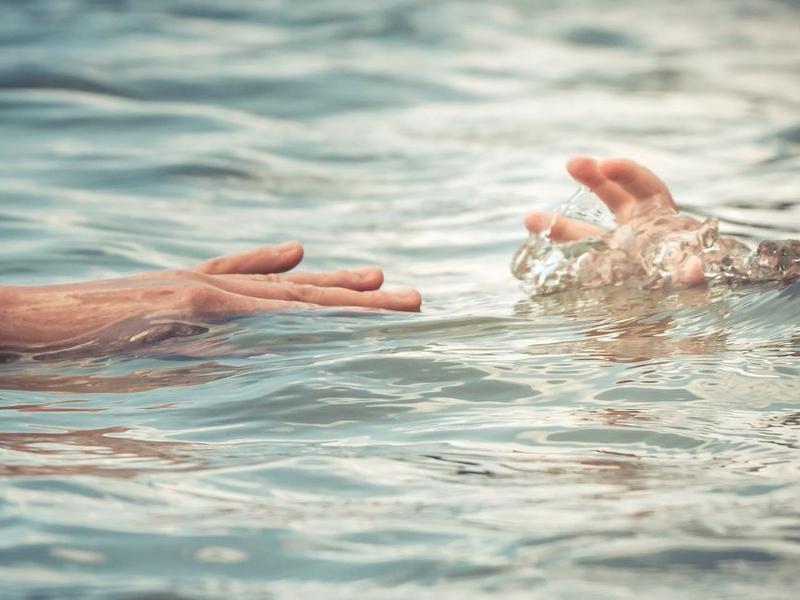 Un adulto intenta alcanzar la mano de un niño que se ahoga