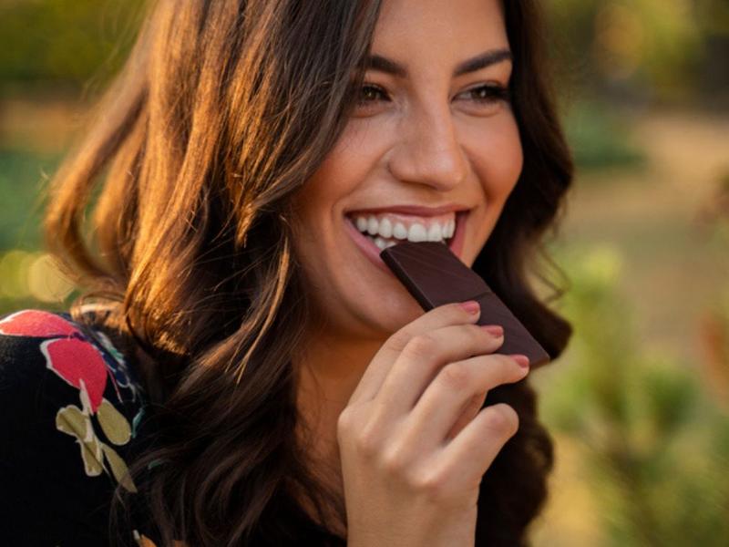 Mujer mordiendo chocolate porque conoce los beneficios