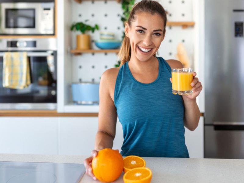 Mujer sonriendo sostiene un vaso de jugo de naranja porque conoce sus beneficios