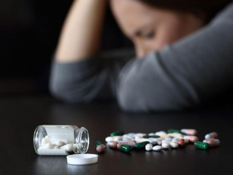 Mujer afligida junto a frasco de pastillas para explicar las adicciones más comunes en mujeres