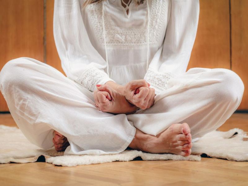 Mujer cruzada de piernas y manos para explicar cómo actúa el kundalini yoga contra el sufrimiento
