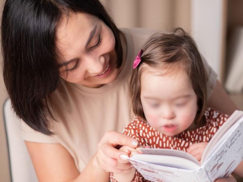 Mujer sosteniendo libro a niña con síndrome de down