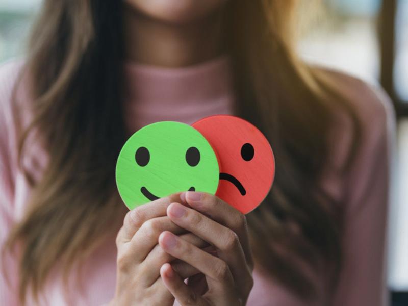 Mujer sosteniendo carita feliz y triste para explicar los signos del trastorno bipolar