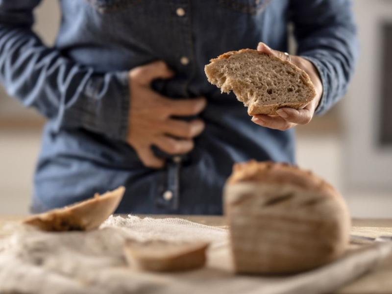 Hombre se agarra el estómago mientras sostiene un pan para explicar los riesgos de una dieta sin gluten