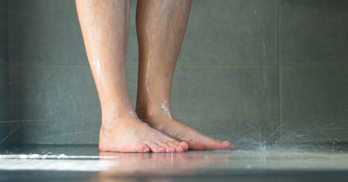 Corte de una persona parada en el baño tomando una ducha.