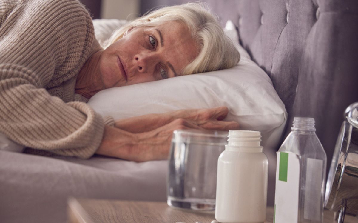 Mujer mayor acostada junto a frasco de pastillas para ilustrar las adicciones más comunes en mujeres