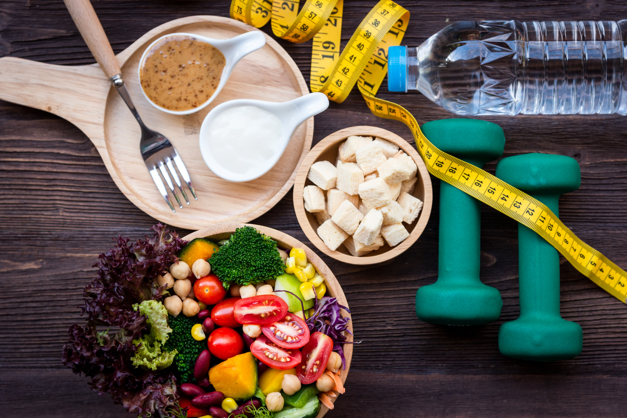 Ensalada, mancuernas, cinta métrica, sobre la mesa, haciendo referencia a los hábitos saludables para bajar niveles de colesterol