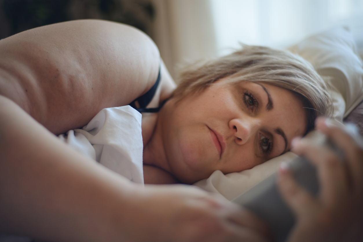 Mujer con sobrepeso revisa su celular en cama
