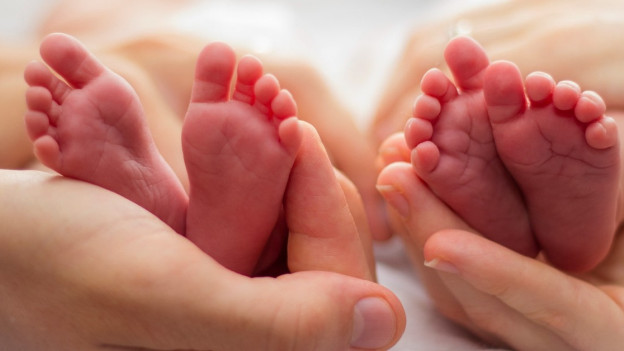 Manos sosteniendo los pies de dos bebés.