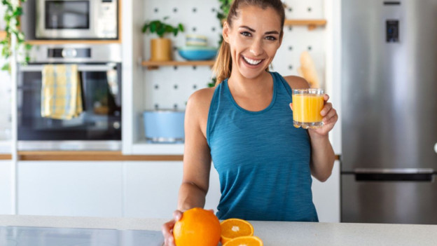 Mujer sonriendo sostiene un vaso de jugo de naranja porque conoce sus beneficios
