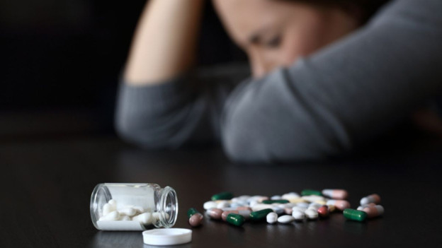 Mujer afligida junto a frasco de pastillas para explicar las adicciones más comunes en mujeres
