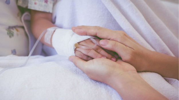Mujer toma mano de su hijo en cama de hospital