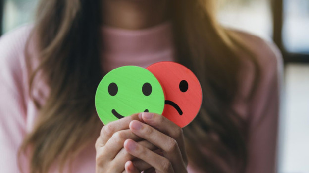 Mujer sosteniendo carita feliz y triste para explicar los signos del trastorno bipolar