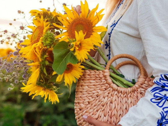 Persona sujetando girasoles y otras flores dentro de un bolso de mimbre.