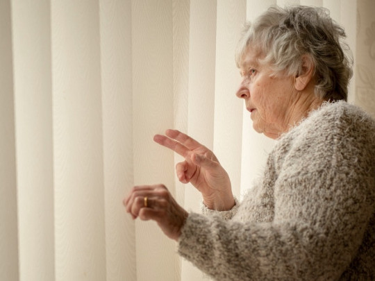 Mujer mayor asomándose a la ventana.