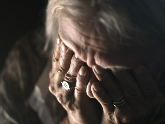 Mujer mayor cubriendo su rostro con ambas manos.