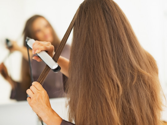 Mujer alisando su cabello con plancha