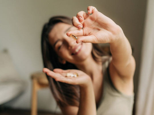 Mujer sosteniendo una píldora para explicar cómo elegir un buen suplemento de vitaminas
