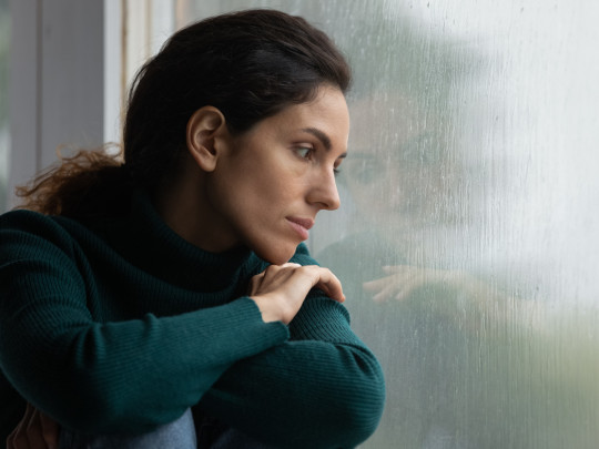 Mujer triste mirando por la ventana para ilustrar las diferencias entre perimenopausia y menopausia