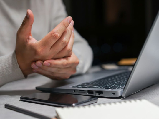 Hombre deteniendo su mano frente a computadora para ilustrar qué es el Parkinson precoz y cuáles son los síntomas clave para detectarlo