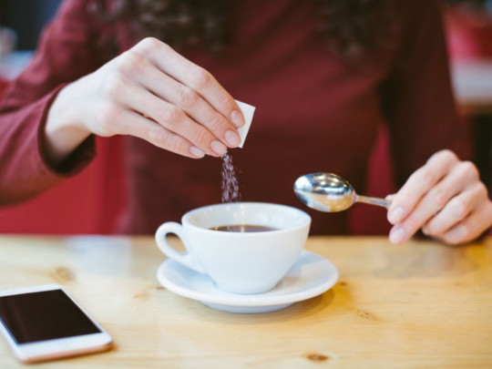 Mujer sirviendo edulcorante en café sin saber que Nuevo edulcorante podría dañar la microbiota y el intestino, revela estudio 
