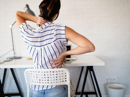 Mujer con dolor en espalda sentada en silla de oficina