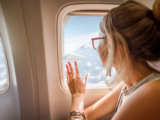 Mujer mirando a través de ventana de avión como motivo a por qué se tapan y destapan los oídos