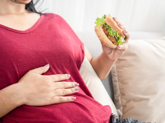 Mujer con hamburguesa se pregunta cuáles son los tres remedios contra la indigestión que dañan tu estómago