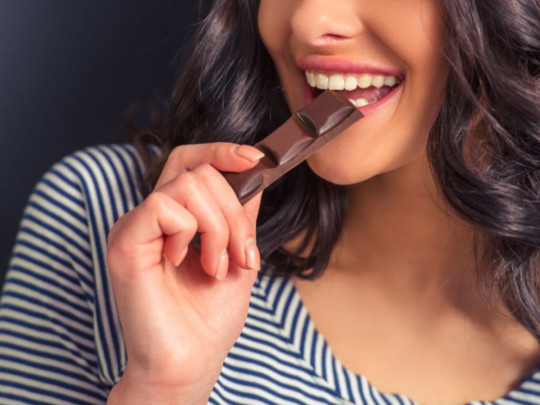 Mujer sonríe mientras come chocolate porque conoce sus beneficios