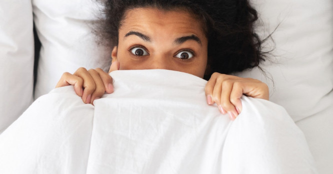 Mujer en la cama con la cara tapada con una sábana.