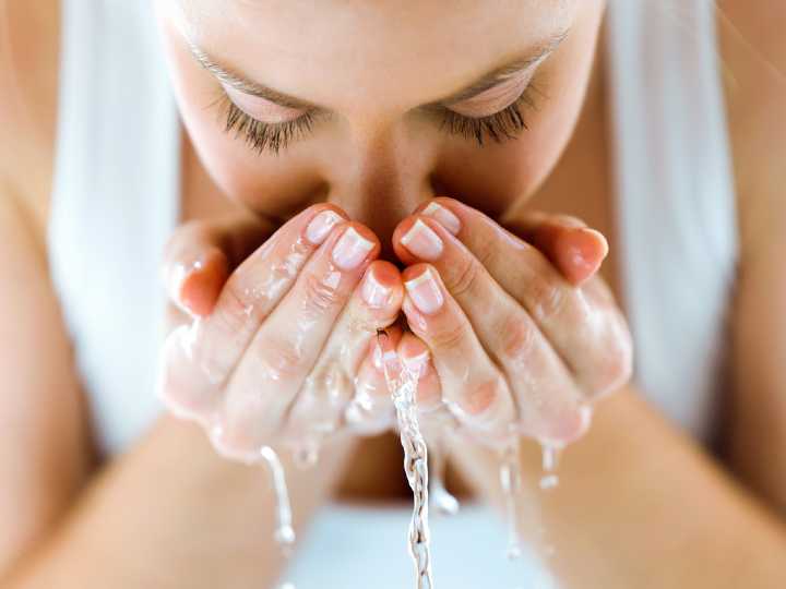 Mujer mojándose el rostro con agua fría para reducir estrés